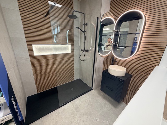 Tiled bay which shows a walk in shower, modern tiles wooden affect alongside a light gray concrete affect tile with a built in niche and light.